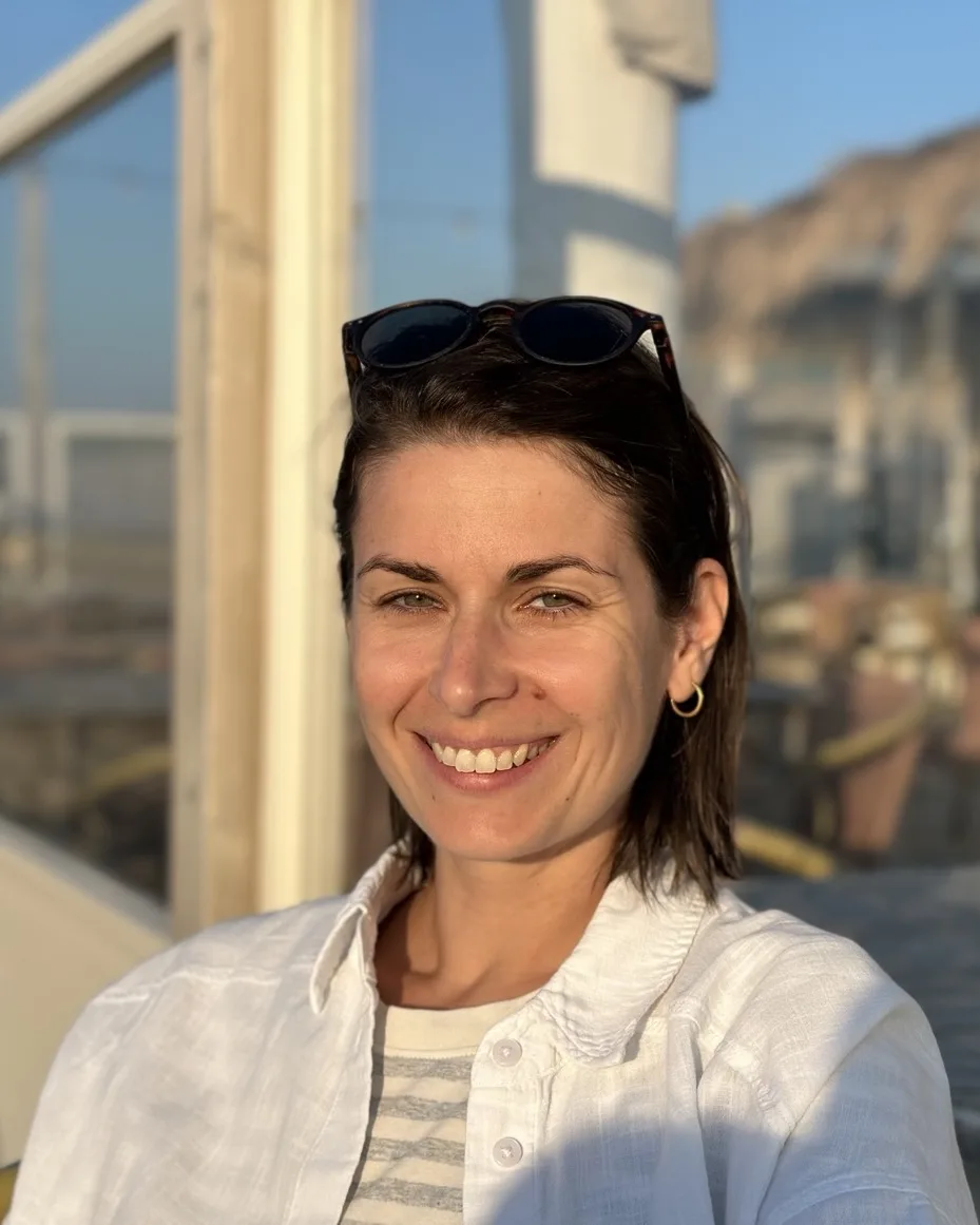 Smiling portrait in a white linen shirt, sunglasses pushed up, on a sunlit terrace